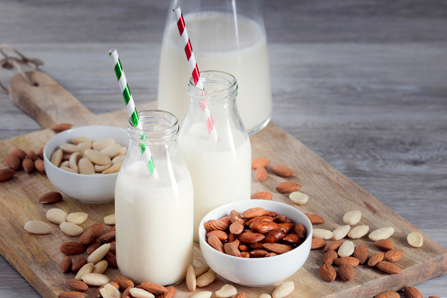 Opskrift på alkoholfri mandelcocktail Stemningsbillede "alkoholfri mandelcocktail": to fyldte flasker med bred hals med farverige sugerør står på en træplade med mandler